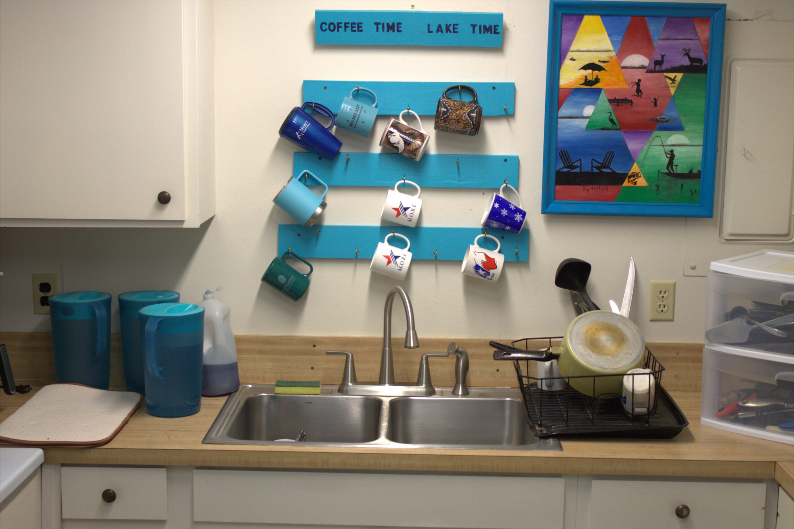 A kitchen with two sinks and cups hanging on the wall.